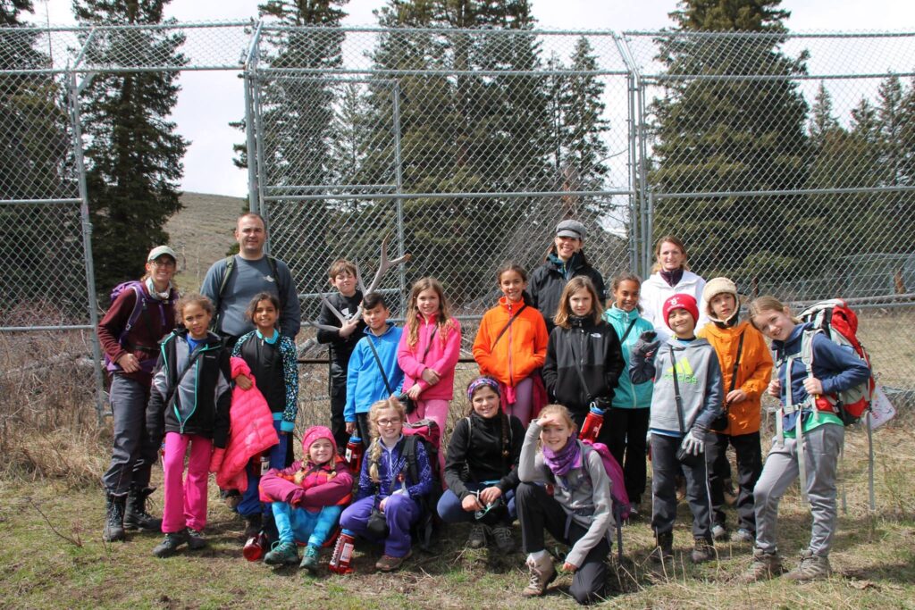 youth educational adventures members posing together by a chainlink fence and holding elk antlers