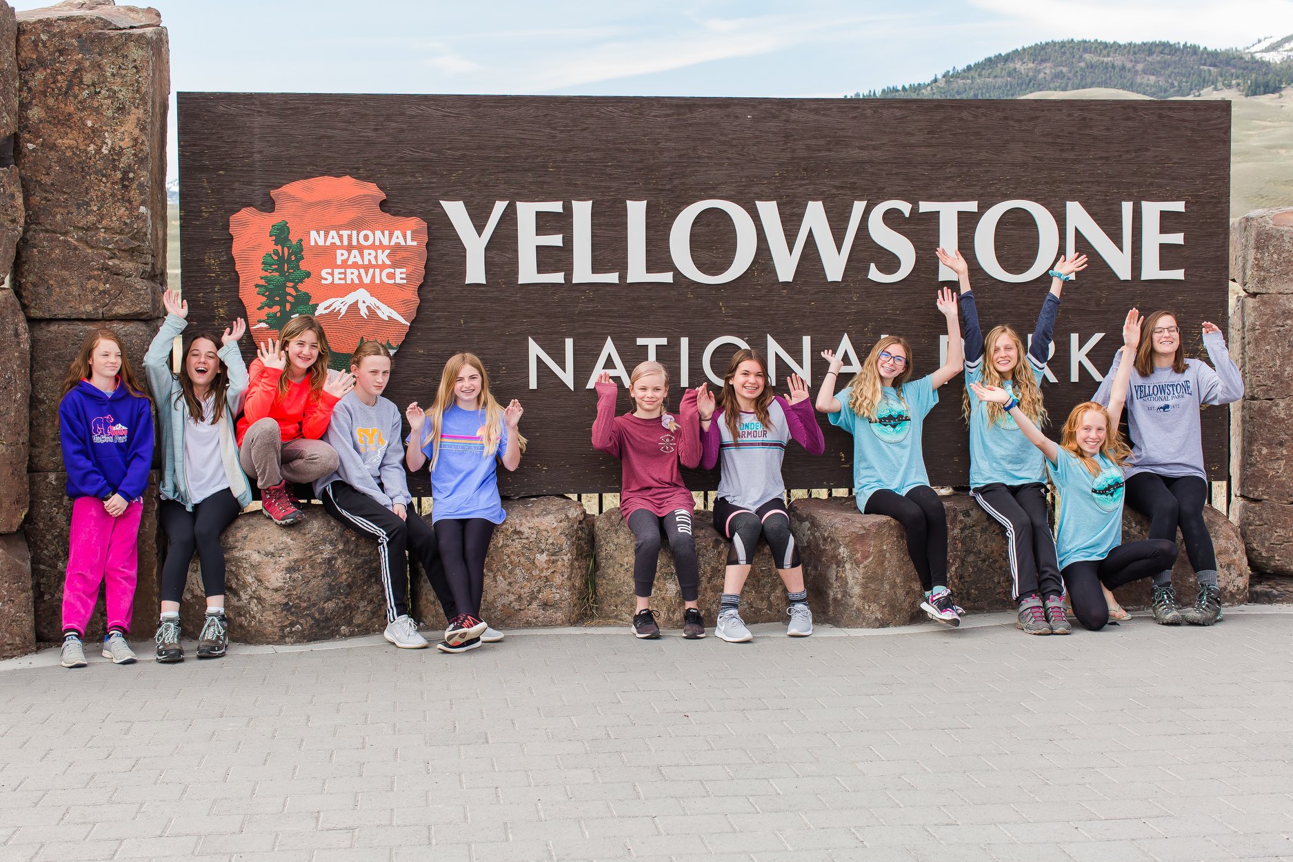 youth educational adventures members posing together in front of the yellowstone national park sign