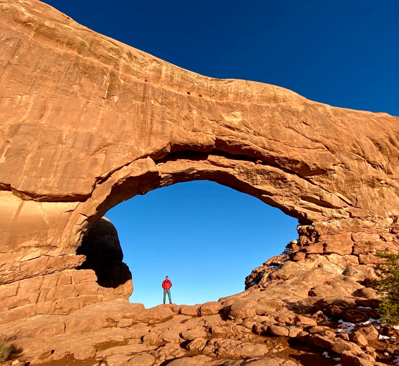 adventure for all member in red jacket standing under a stone archway at the utah big 5