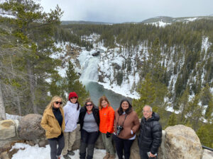 adventures for all group posing by stone wall above a waterfall and snow covered forest landscape