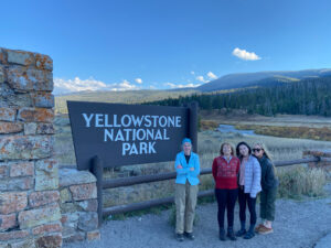 4 adventures for all group members posing in front of the Yellowstone National Park sign