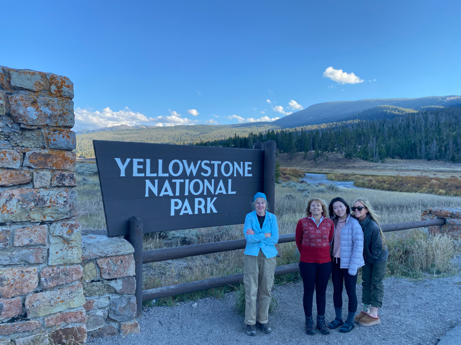 4 adventures for all group members posing in front of the Yellowstone National Park sign