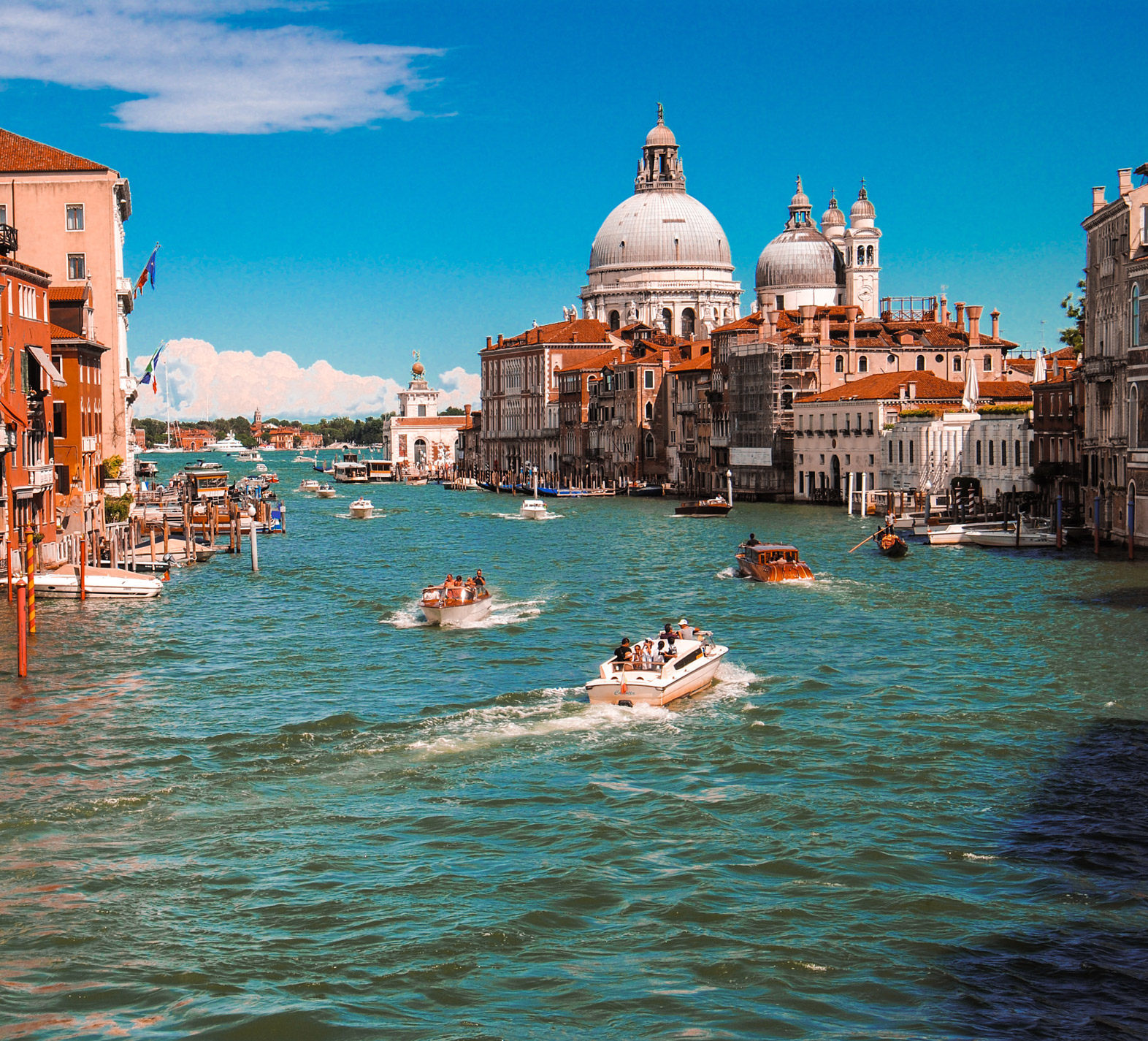 boats moving through italy on blue waters surrounded by brick colored buildings