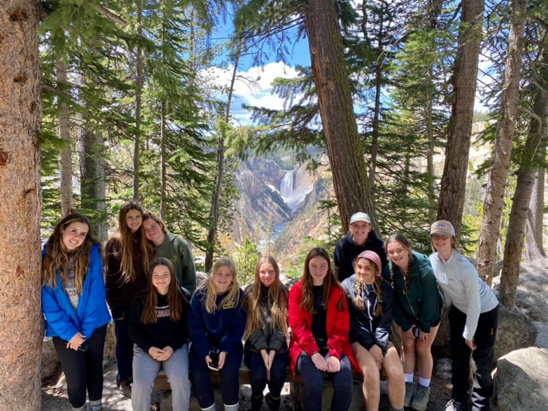youth educational adventures group posing by trees in front of distant mountains and a waterfall