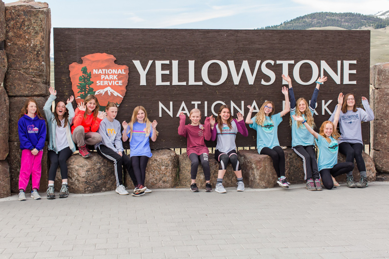 youth educational adventures group cheering in front of a yellowstone national park sign