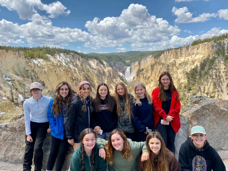 youth educational adventures group smiling in front of a distant waterfall in yellowstone national park