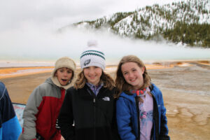 three youth educational adventure members huddled together and smiling by hot springs