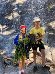 two youth educational adventurers smiling and holding rock climbing equipment